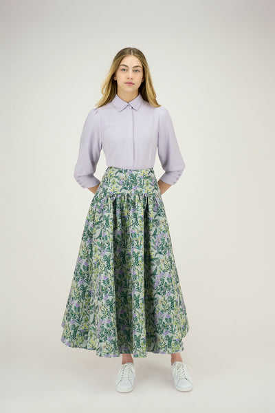 Woman wearing a light purple shirt and floral skirt on a white background