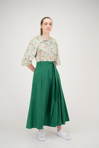 Woman wearing a floral blouse and green skirt on a white background