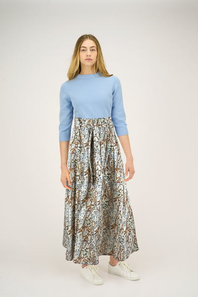 Woman wearing a light blue sweater and patterned skirt on a white background