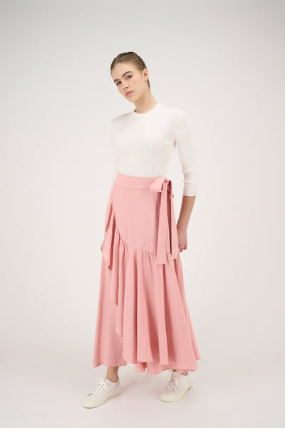 Woman wearing a white top and pink skirt on a white background